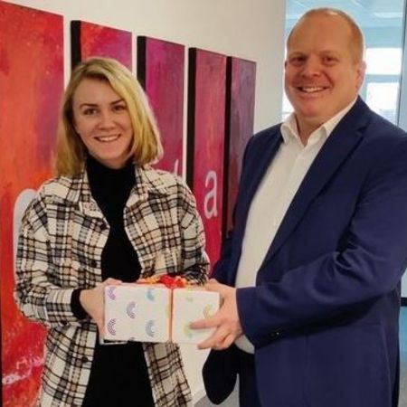 Frau bekommt Geschenk von Mann im Büroflur mit Kunst