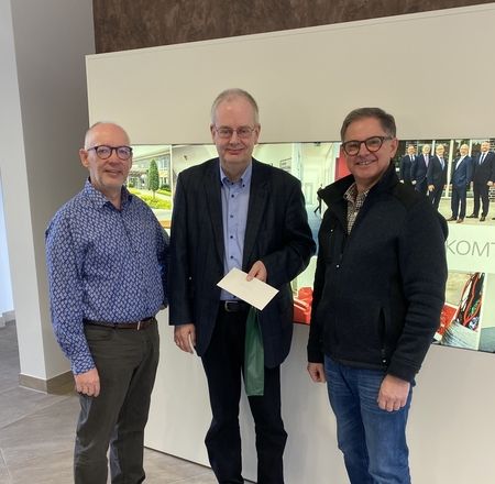 Drei Männer mit Umschlag und Geschenk vor Firmenwand