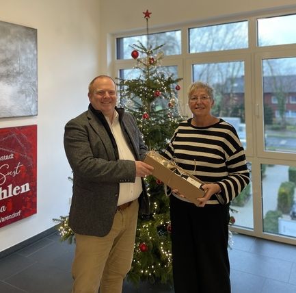 Mann überreicht Frau ein Geschenk vor Weihnachtsbaum