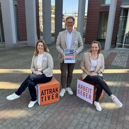Drei Personen mit Auszeichnung auf Würfeln „Attraktiver Arbeitgeber“.