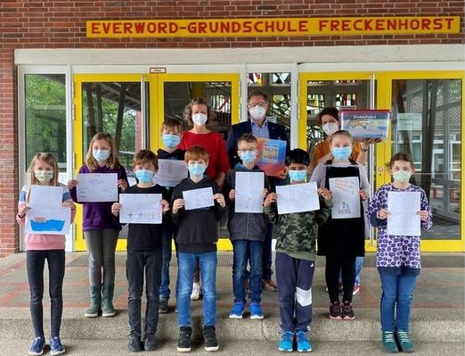 Schulklasse mit Masken zeigt Bilder vor Schuleingang