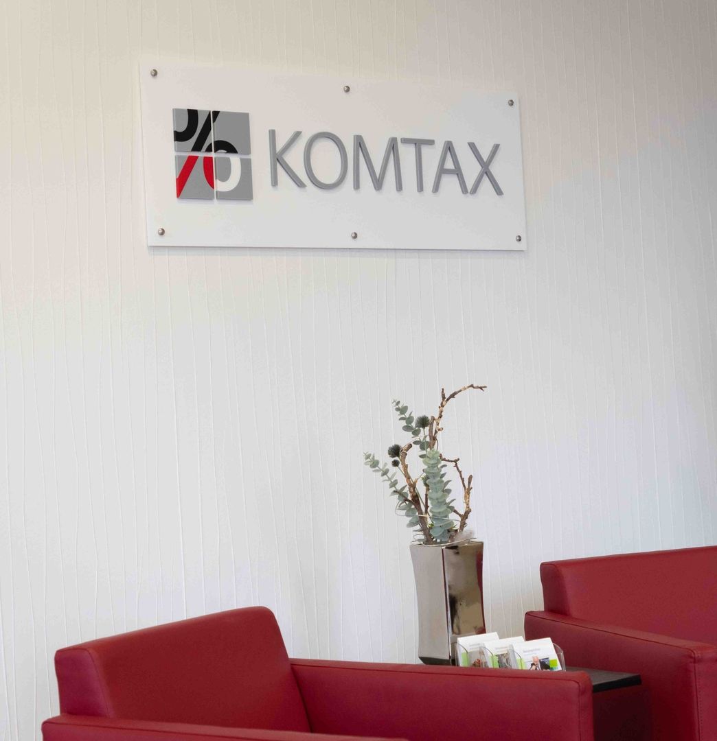 Ein roter Sessel vor einer hellen Wand mit dem Komtax Logo