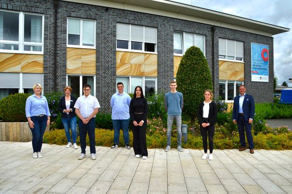 Acht Personen vor moderner Gebäudefassade, Gruppenfoto