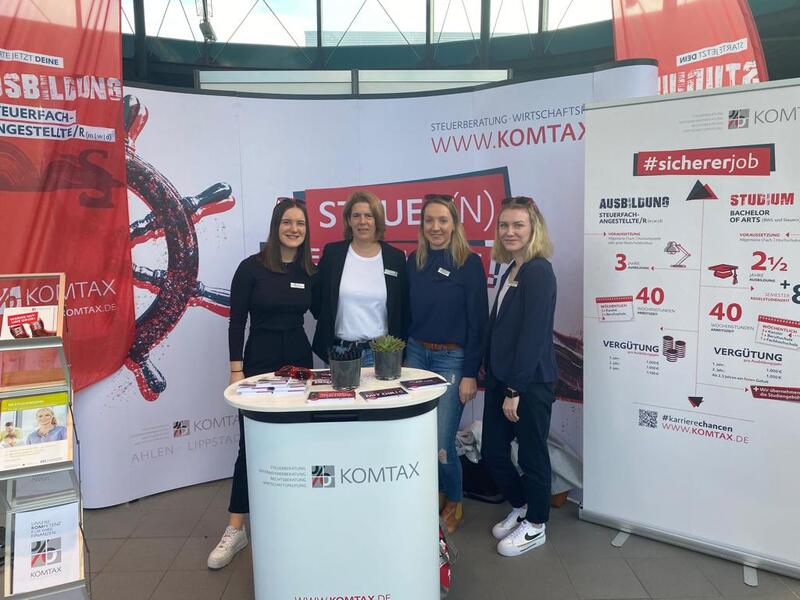 Vier Frauen am KOMTAX-Messestand mit Infomaterial