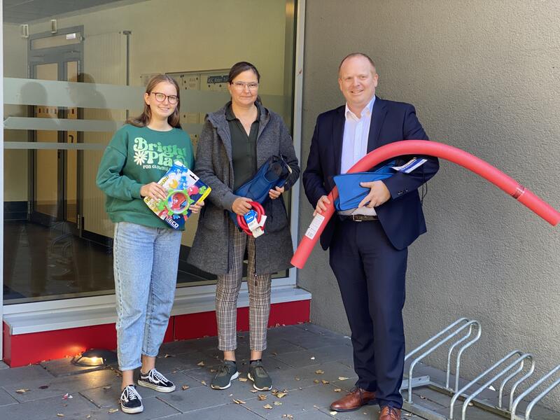 Zwei Frauen und ein Mann mit Schwimmutensilien vor Eingang